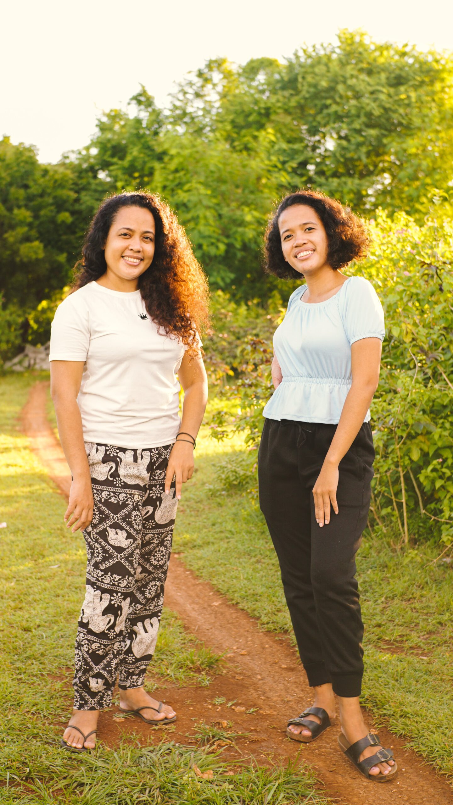 Smiling women with curly hair posing together outdoors on a sunny day.